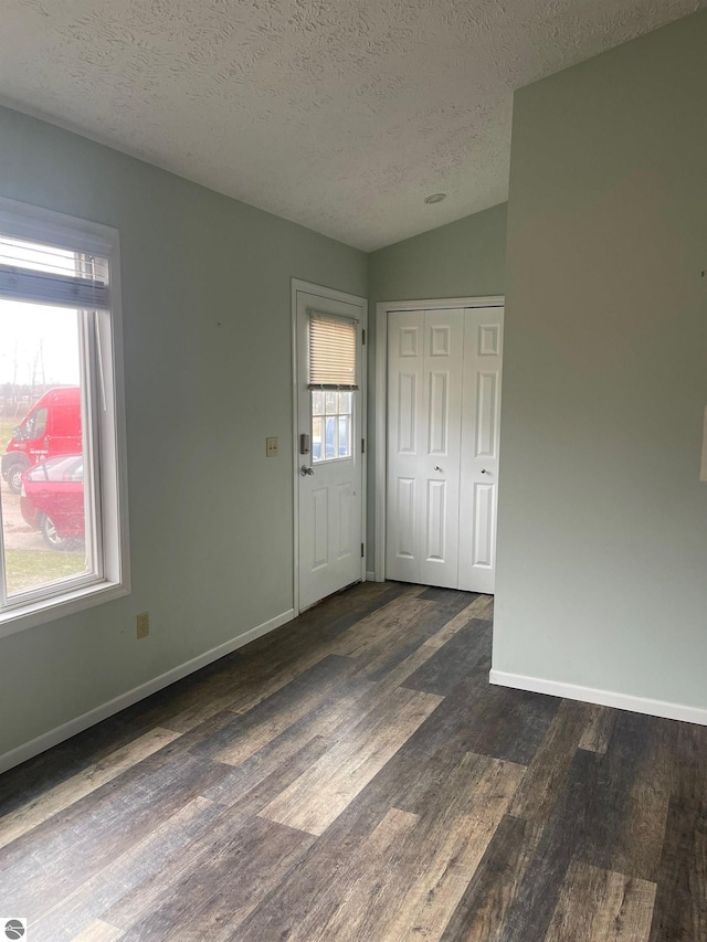 empty room featuring vaulted ceiling, dark wood-type flooring, and a textured ceiling