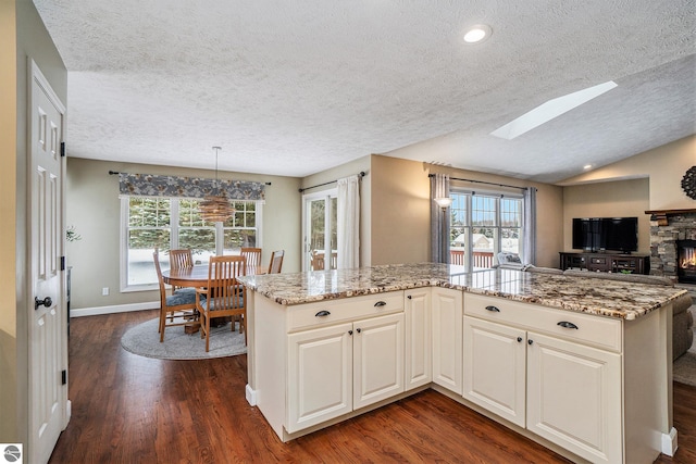 kitchen featuring light stone counters, a wealth of natural light, open floor plan, and dark wood-style floors