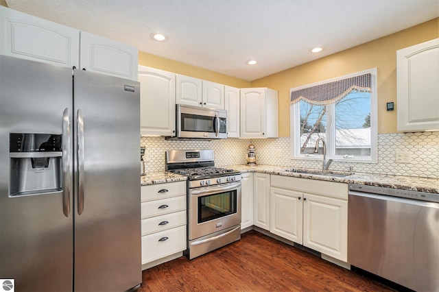 kitchen with light stone countertops, dark wood finished floors, a sink, stainless steel appliances, and white cabinets