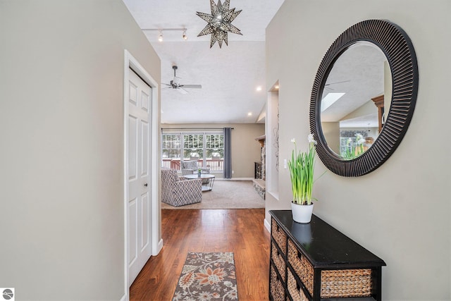 corridor with baseboards, lofted ceiling, wood finished floors, and rail lighting