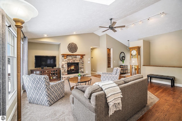 living room featuring wood finished floors, baseboards, a ceiling fan, a fireplace, and vaulted ceiling