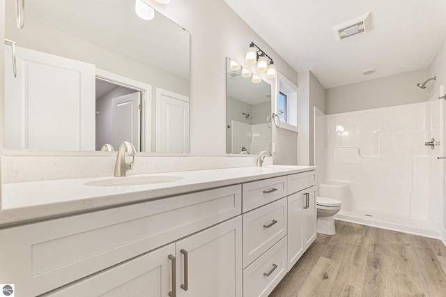 bathroom with walk in shower, hardwood / wood-style floors, vanity, and toilet