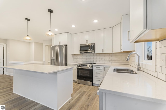 kitchen with sink, hanging light fixtures, stainless steel appliances, a center island, and white cabinets