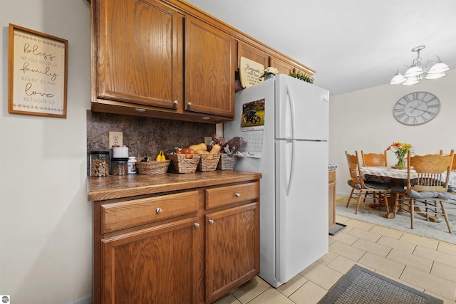 kitchen with tasteful backsplash, an inviting chandelier, hanging light fixtures, light tile patterned floors, and white fridge