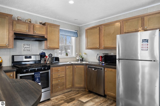 kitchen featuring stainless steel appliances, crown molding, wood-type flooring, and sink