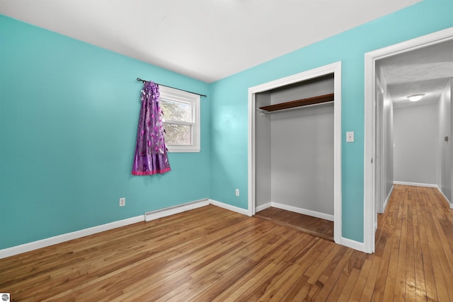 unfurnished bedroom with wood-type flooring, a closet, and baseboard heating