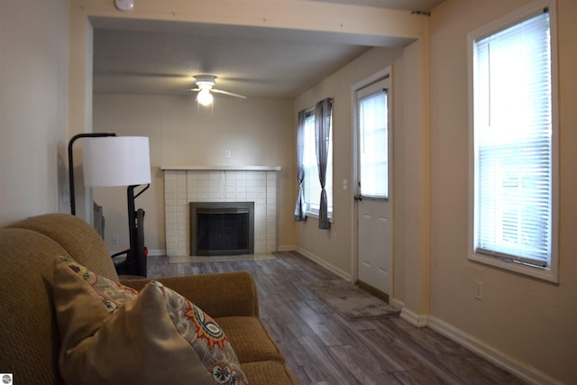 living room with a tiled fireplace, dark wood-type flooring, and ceiling fan