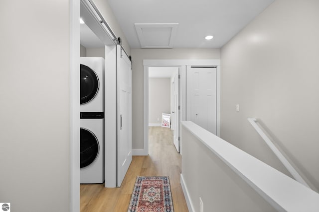 clothes washing area with stacked washer and dryer, a barn door, and light wood-type flooring