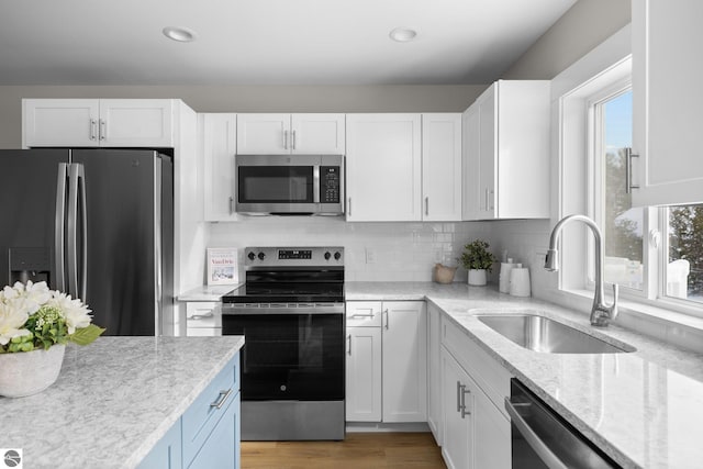 kitchen with appliances with stainless steel finishes, sink, white cabinets, light stone countertops, and light hardwood / wood-style flooring