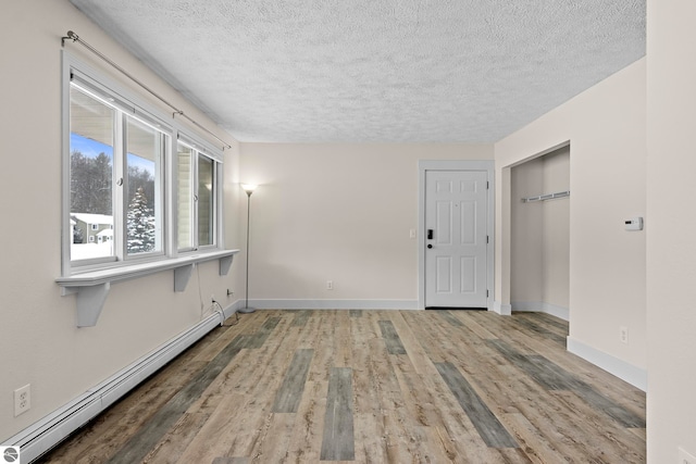 empty room featuring hardwood / wood-style flooring, a textured ceiling, and a baseboard heating unit