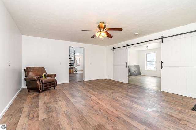 sitting room with wood-type flooring, a barn door, and ceiling fan