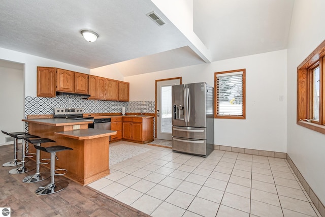 kitchen featuring light tile patterned flooring, appliances with stainless steel finishes, a kitchen breakfast bar, and kitchen peninsula