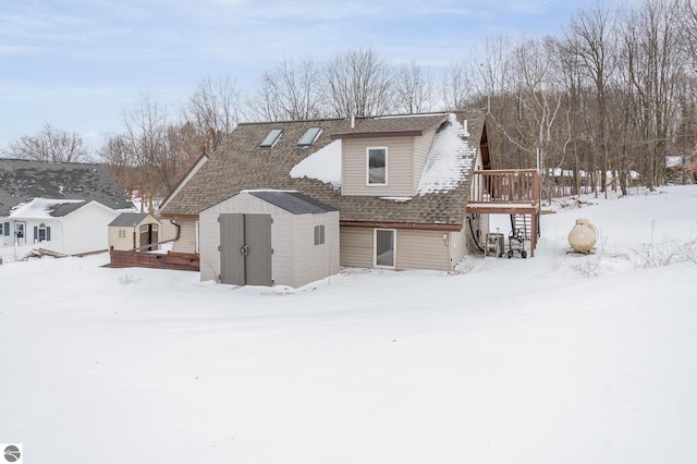 snow covered property with a wooden deck and a storage shed