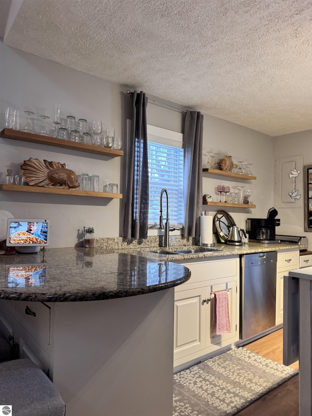 kitchen with wood-type flooring, sink, stainless steel dishwasher, and dark stone counters