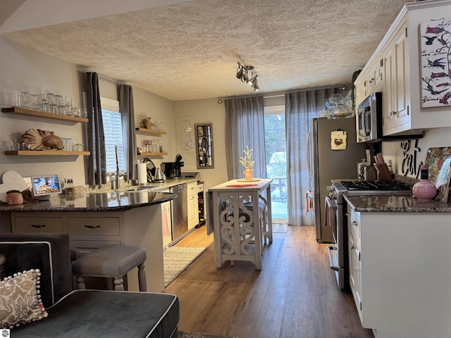 kitchen featuring white cabinetry, wood-type flooring, sink, dark stone counters, and stainless steel appliances