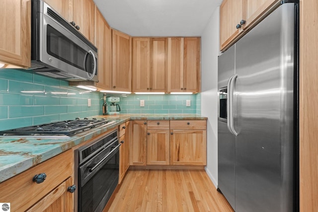 kitchen featuring light brown cabinetry, tasteful backsplash, light stone counters, appliances with stainless steel finishes, and light hardwood / wood-style floors