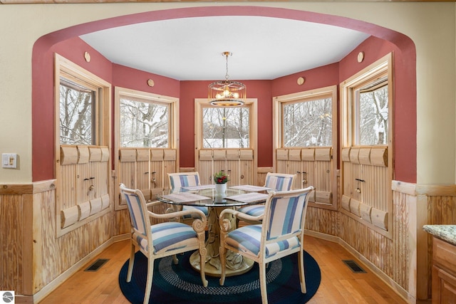 dining area with wooden walls, a notable chandelier, and light wood-type flooring