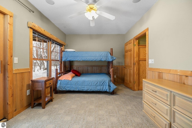 bedroom with ceiling fan, light colored carpet, and wooden walls