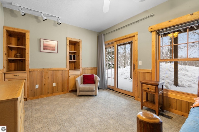 sitting room featuring ceiling fan, light colored carpet, a textured ceiling, and wood walls