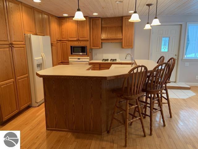 kitchen with white appliances, a center island with sink, hanging light fixtures, and light wood-type flooring