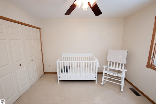 carpeted bedroom with a nursery area, ceiling fan, and a closet