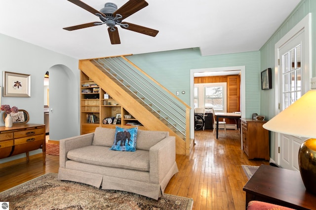 living room with baseboard heating, ceiling fan, wood-type flooring, and built in shelves