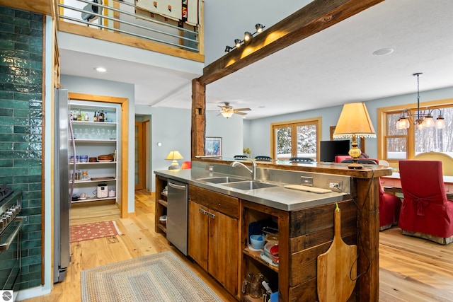 kitchen featuring appliances with stainless steel finishes, ceiling fan with notable chandelier, decorative light fixtures, sink, and light hardwood / wood-style floors