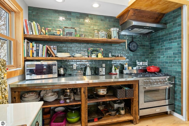 bar with light hardwood / wood-style flooring, stainless steel counters, stainless steel appliances, tasteful backsplash, and wall chimney exhaust hood