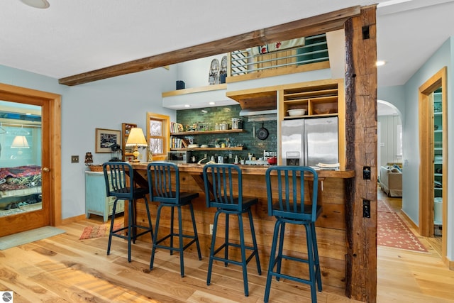 bar with beamed ceiling, backsplash, stainless steel fridge, and light wood-type flooring