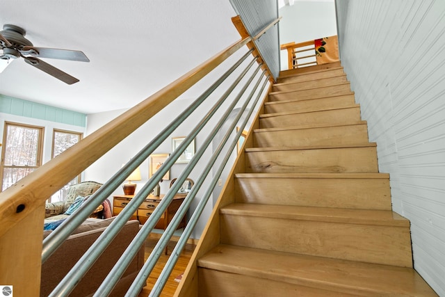 stairs with ceiling fan and wood walls