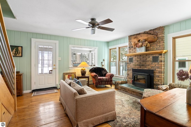 living room with ceiling fan, light hardwood / wood-style floors, a brick fireplace, and a baseboard heating unit