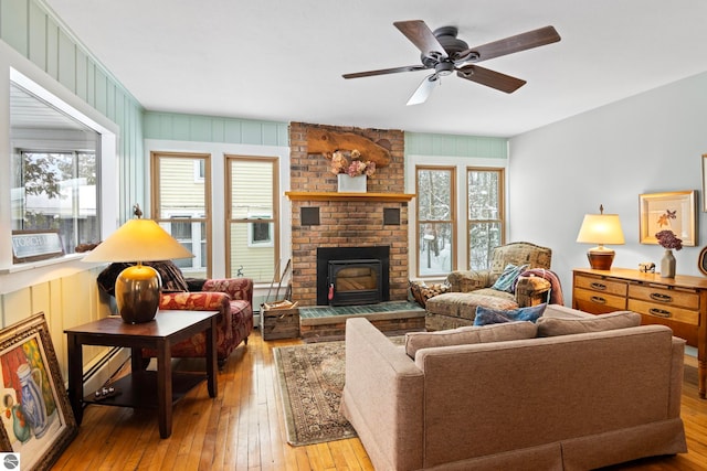 living room featuring a brick fireplace, light hardwood / wood-style floors, ceiling fan, and a baseboard heating unit