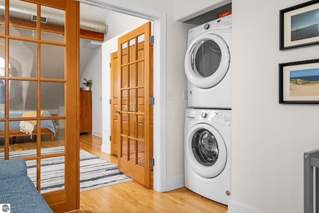 clothes washing area with stacked washer and clothes dryer and light hardwood / wood-style flooring