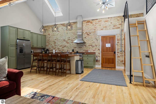 living room with a skylight, brick wall, light hardwood / wood-style floors, and high vaulted ceiling