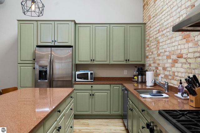 kitchen featuring sink, green cabinetry, hanging light fixtures, appliances with stainless steel finishes, and brick wall