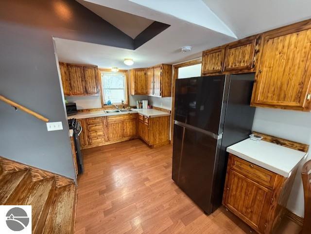 kitchen with vaulted ceiling, sink, gas range, black fridge, and light wood-type flooring