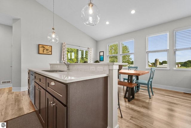 kitchen featuring vaulted ceiling, sink, hanging light fixtures, dark brown cabinetry, and light hardwood / wood-style floors