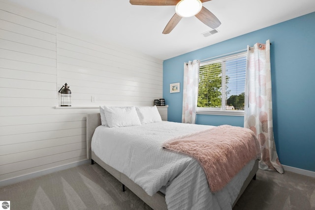 carpeted bedroom with ceiling fan and wood walls