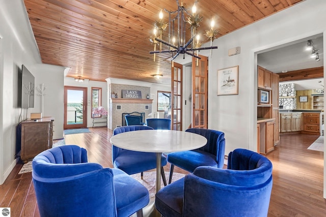 dining area featuring wood-type flooring, an inviting chandelier, wooden ceiling, and a fireplace