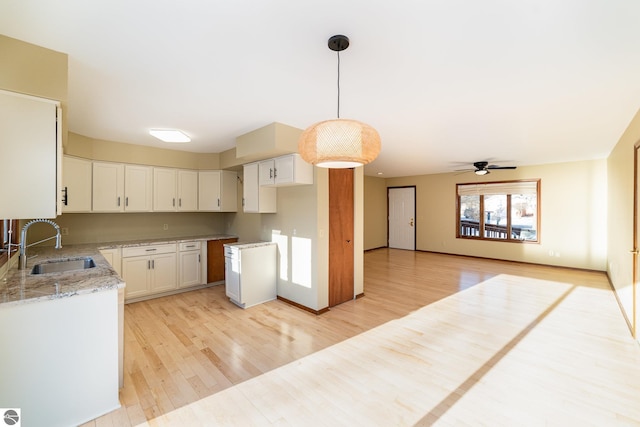 kitchen featuring white cabinetry, sink, hanging light fixtures, light stone countertops, and light wood-type flooring