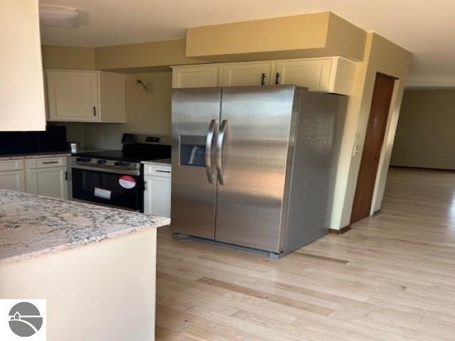 kitchen with white cabinets, light stone counters, light wood-type flooring, and appliances with stainless steel finishes