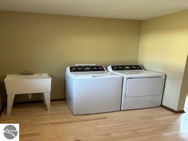 clothes washing area featuring laundry area, independent washer and dryer, light wood-type flooring, and baseboards