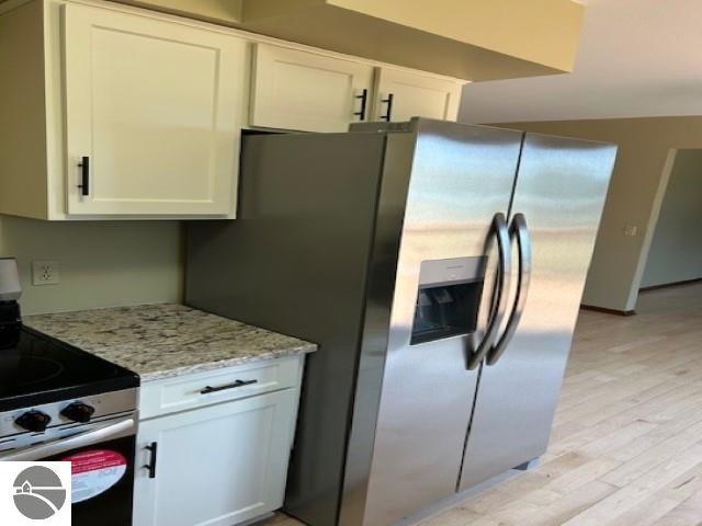 kitchen with stainless steel appliances, light stone countertops, light wood-style floors, and white cabinetry