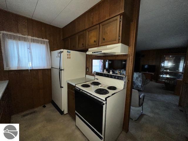 kitchen with white appliances, wooden walls, and carpet flooring