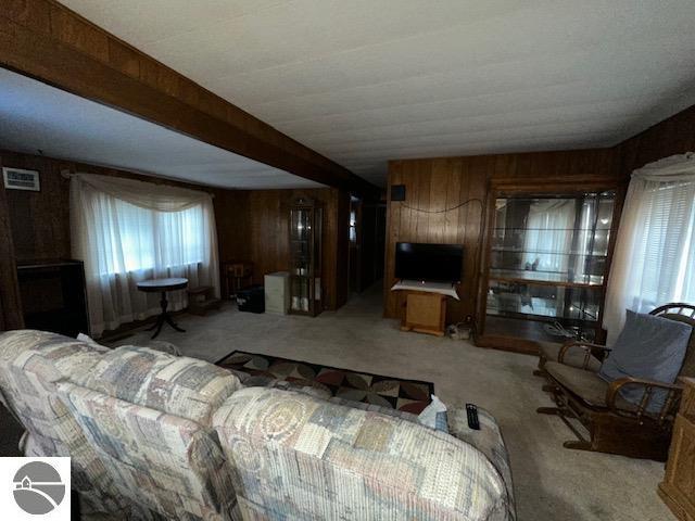 carpeted living room with beam ceiling and wooden walls