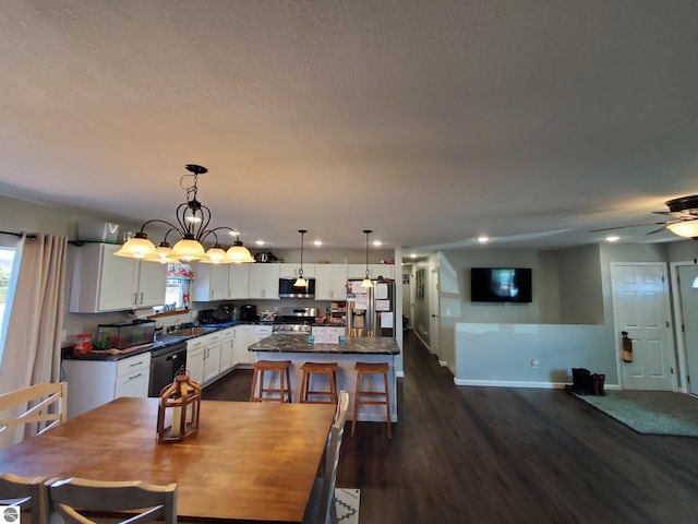 dining space featuring ceiling fan with notable chandelier, sink, and dark wood-type flooring