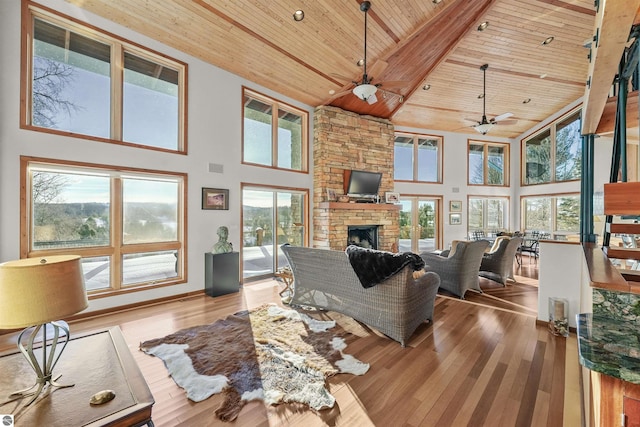 living room with wooden ceiling, a stone fireplace, a wealth of natural light, and light wood-type flooring