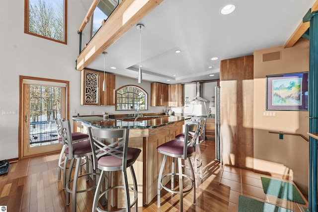 kitchen featuring pendant lighting, dark stone countertops, a kitchen breakfast bar, wall chimney range hood, and light wood-type flooring