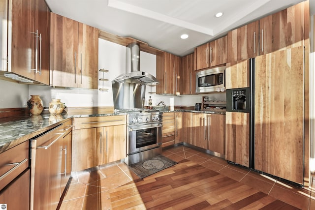 kitchen featuring appliances with stainless steel finishes, ventilation hood, dark tile patterned flooring, and dark stone countertops