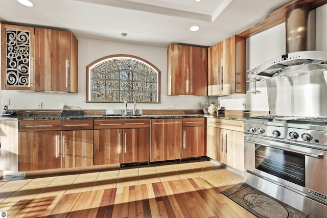 kitchen with sink, light hardwood / wood-style flooring, dark stone countertops, stainless steel appliances, and wall chimney range hood